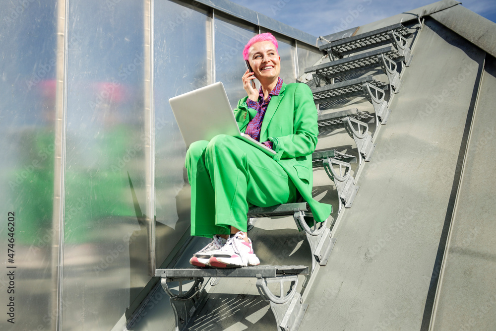 Smiling businesswoman talking through smart phone sitting on staircase at rooftop