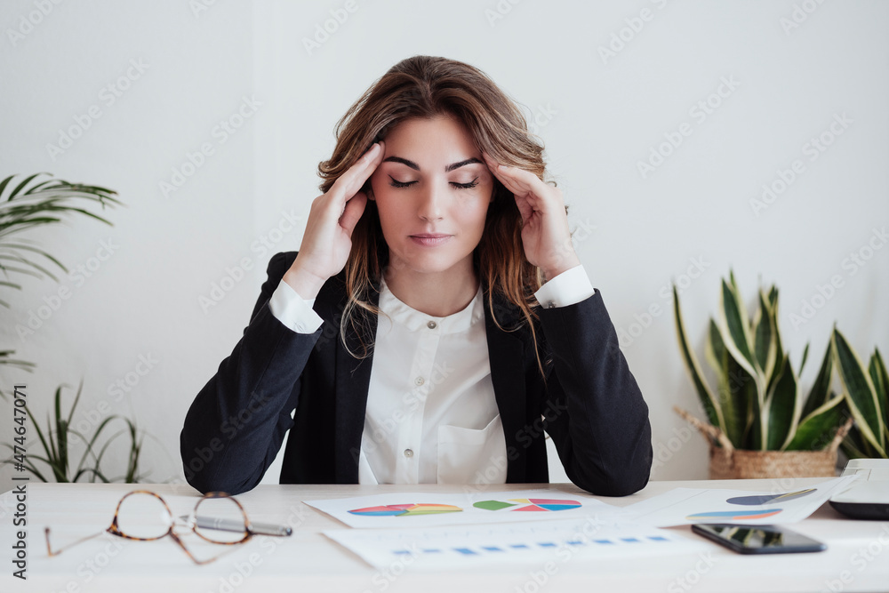 Tired businesswoman with head in hands sitting at desk in office