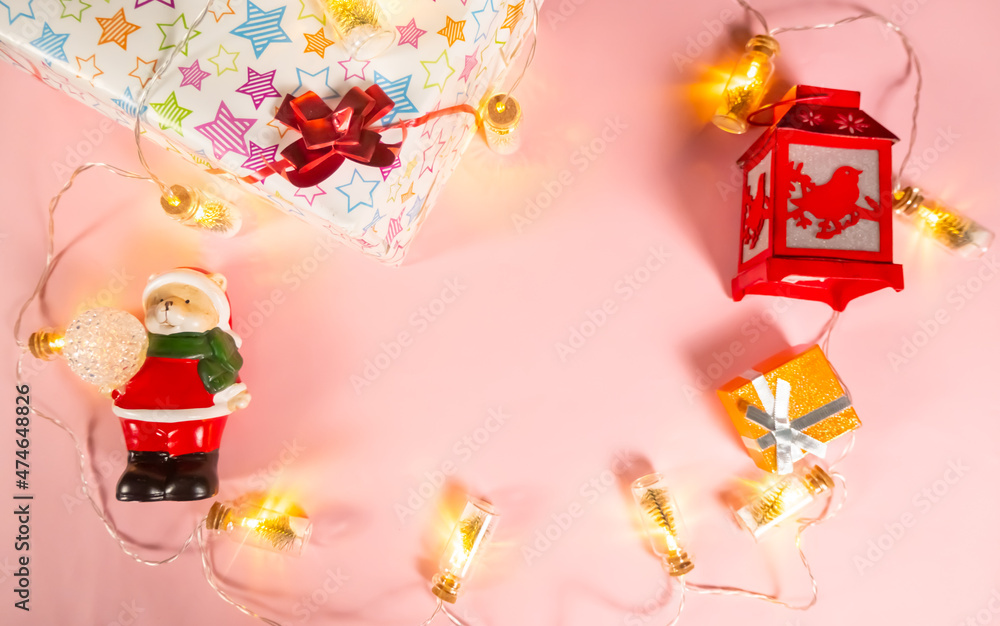 Christmas background - Christmas decorations - a garland, a gift box, a flashlight and a bear in a Santa Claus costume on a light pink background, copy the space.