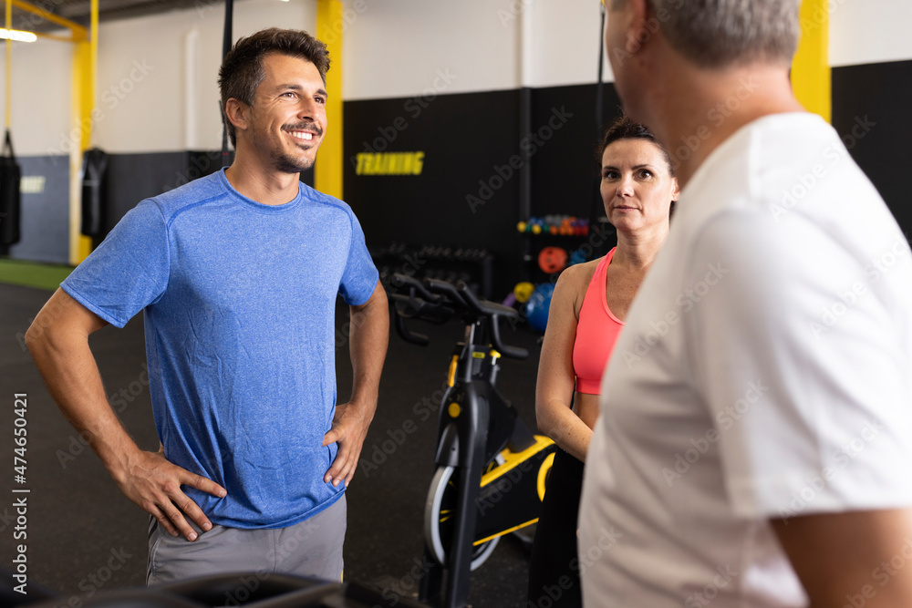 Smiling sportsman with hand on hip talking with friends in gym Smiling sportsman with hand on hip talking with friends in gym