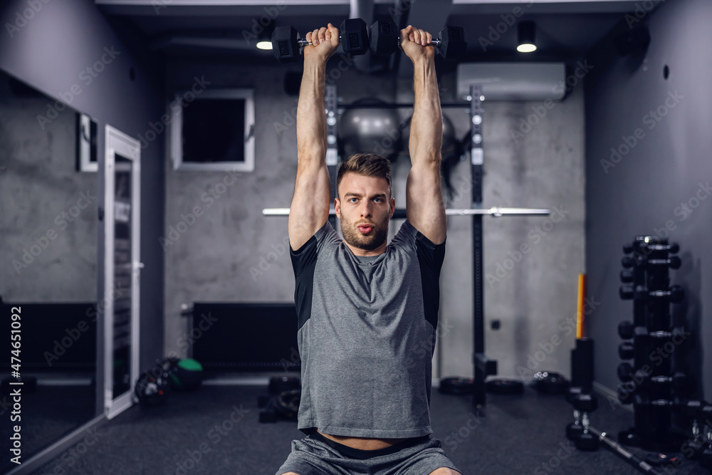 Fototapeta premium The athlete trains dumbbells in the gym on a dark grey background. Sport concept and taking care of the figure. The man lifts dumbbells, cares for his muscles. Weightlifting, sports training