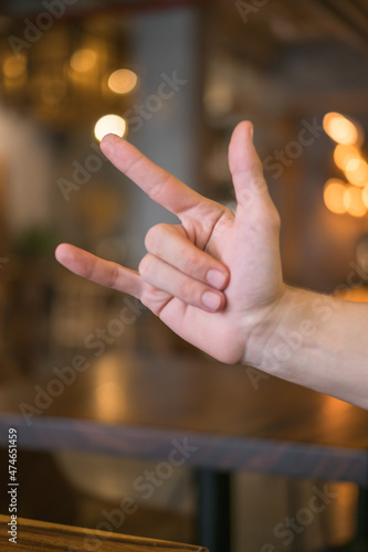 Male hand close-up on brown background with lamps shows hand gesture. Rock'n'roll. Rock hand sign. High quality photo