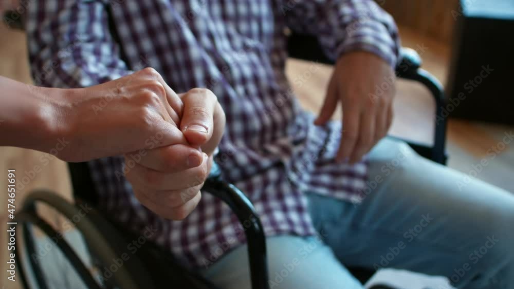 Disabled man in wheelchair holds his wifes hand. Disabled person holds hand of loved one who supported him. Concept of family and support Disabled man in wheelchair holds his wifes hand. Disabled person holds hand of loved one who supported him. Concept of family and support