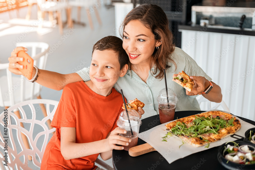 Mother and son have a good time in a cafe eating pizza and taking selfies on a smartphone for social networks