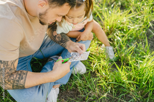 Curious girl sitting by father cutting transferable tattoos on grass photo