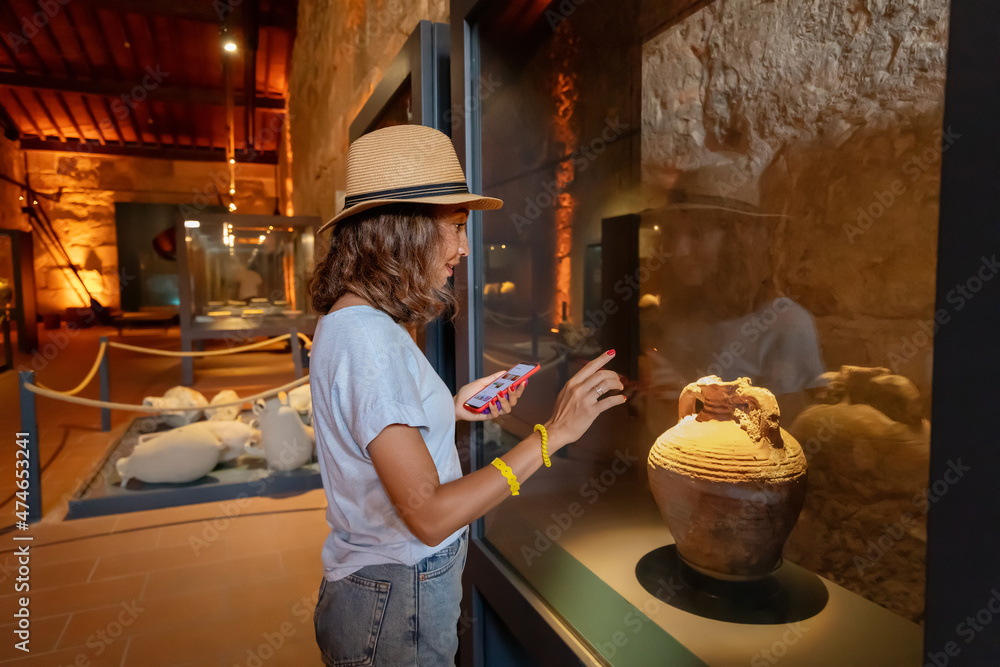 Visitor woman using smartphone with audio guide app to know about ancient greek artifacts and exhibits
