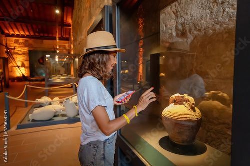 Visitor woman using smartphone with audio guide app to know about ancient greek artifacts and exhibits