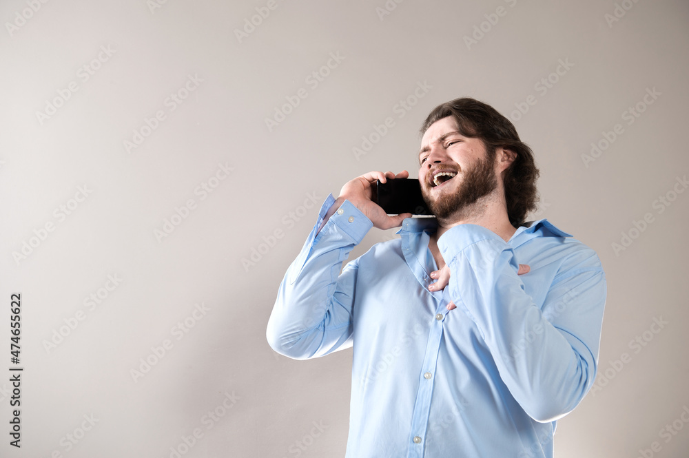 Young bearded man having call and talking on smartphone with pleasure isolated over grey background Young bearded man having call and talking on smartphone with pleasure isolated over grey background