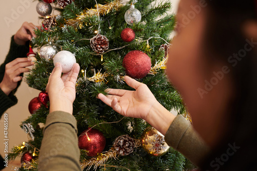 Hands of senior woman hanging colorful sparkling baubles on Christmas tree