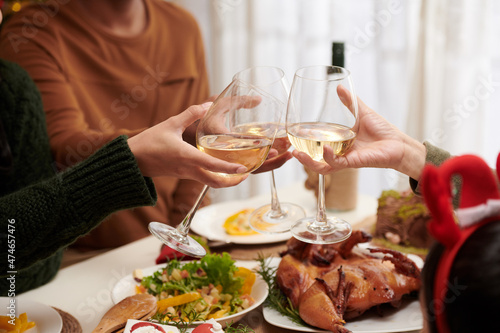 Party guests clinking glasses with white wine over Christmas dinner table