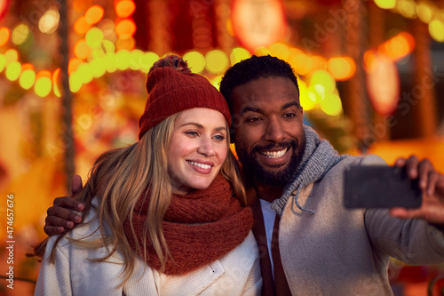 Couple Against City Lights Outdoors Wearing Coats And Scarves Posing For Selfie On Phone In Autumn
