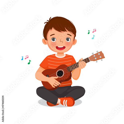 Cute little boy playing ukulele singing holding a guitar with smiling facial expression