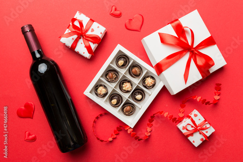 Bottle of red wine on colored background for Valentine Day with gift and chocolate. Heart shaped with gift box of chocolates top view with copy space © sosiukin