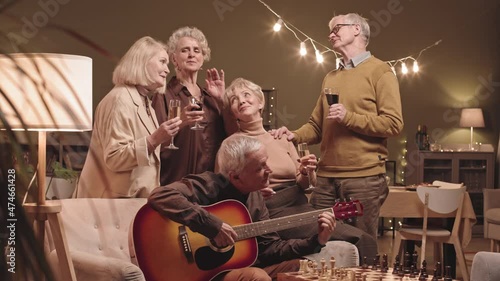 Wallpaper Mural Medium slowmo shot of five happy senior men and women with glasses of red wine and champagne singing songs while their friend playing guitar, sitting together on sofa at cozy living room in evening Torontodigital.ca