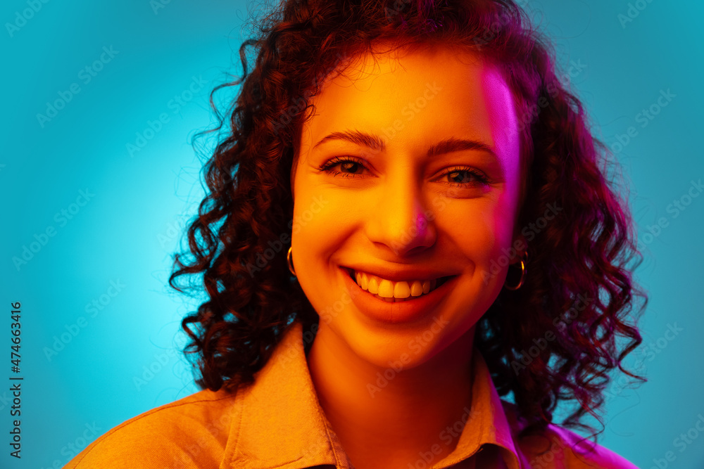 Close-up young beautiful cheerful girl smiling isolated on blue studio background in neon light.
