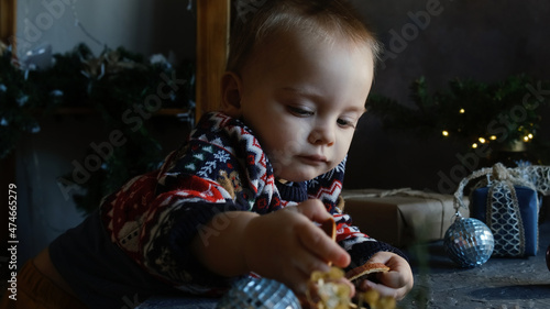 Adorable little boy in Christmas sweater touching Christmas ornaments surrounded by Xmas interior and decorations at home. Holiday home decorating  domestic life  Xmas preparation concept.