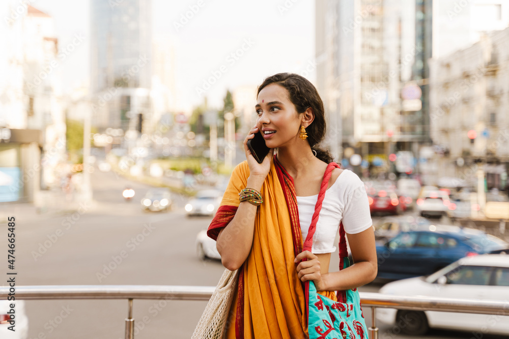 Fototapeta premium Young indian woman wearing sari talking on cellphone at city street