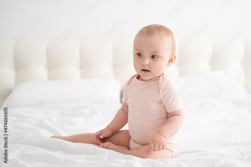 portrait of baby girl 10 months in light pink bodysuit on white bedding on bed portrait of baby girl 10 months in light pink bodysuit on white bedding on bed