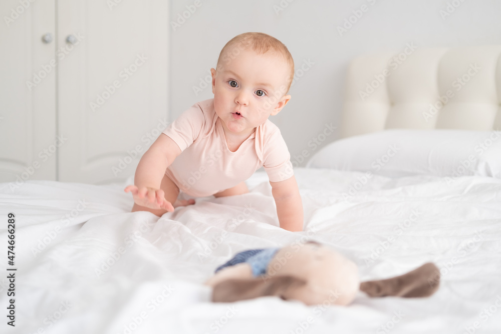 baby girl in light pink bodysuit playing with soft toy on white bedding on bed baby girl in light pink bodysuit playing with soft toy on white bedding on bed
