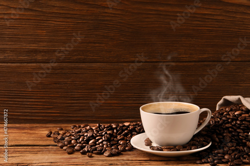 Cup of aromatic hot coffee and beans on wooden table, space for text
