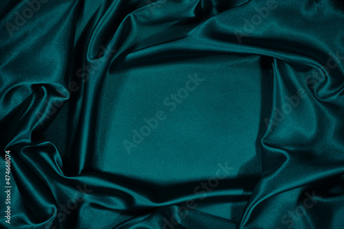 Green silk satin velvet. Wavy soft folds. Smooth. Shiny fabric. Luxurious dark teal background with copy space for design. Table top view. Flat lay. Empty. Template.