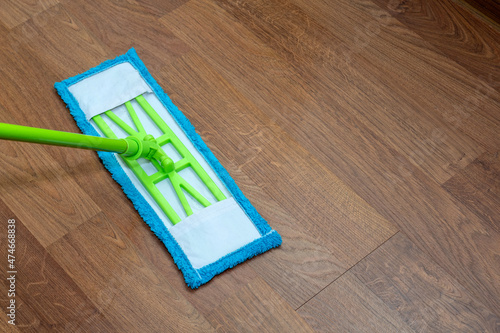 Green mop with blue nozzle washes the laminate. Selective focus. Picture for articles about cleanliness, cleaning.