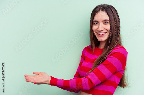 Young caucasian woman isolated on green background holding a copy space on a palm.