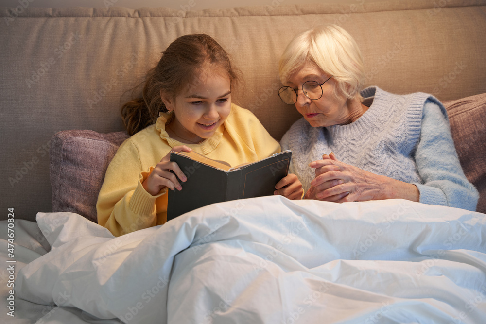 Radiant little girl enjoying bed story time with her grandma Radiant little girl enjoying bed story time with her grandma