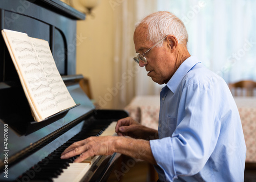 Grandfather is learning to play piano at home. Life after retirement concept © caftor
