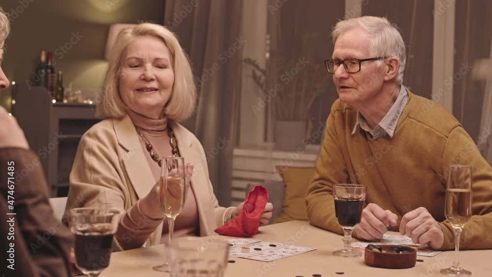 Waist up slowmo shot of cheerful group of seniors sitting at festive dinner table in evening playing game of Bingo and spending good time together Waist up slowmo shot of cheerful group of seniors sitting at festive dinner table in evening playing game of Bingo and spending good time together