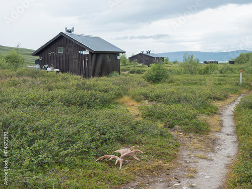 View of mountain hut STF Laddejahka fjallstuga cabin with moose antlers lying next to path. Lapland landscape Sweden at Padjelantaleden hiking trail. Summer moody sky photo
