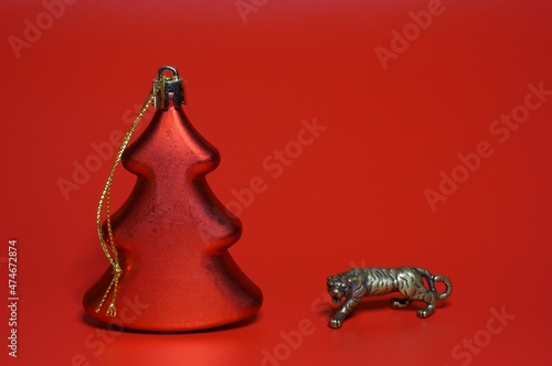 A metal tiger figurine and a Christmas tree on a red background.