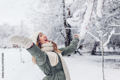 Happy young woman playing with snow in snowy winter park wearing warm knitted clothes and having fun Fototapet
