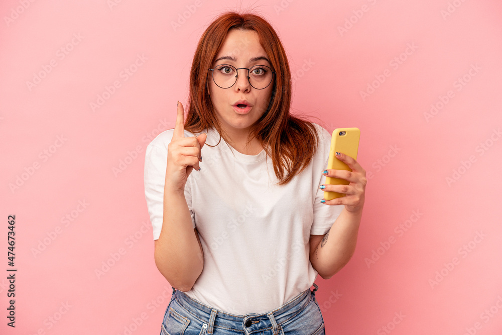 Young caucasian woman holding a mobile phone isolated on pink background having some great idea, concept of creativity. Young caucasian woman holding a mobile phone isolated on pink background having some great idea, concept of creativity.