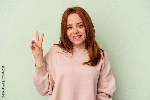 Wallpaper Mural Young caucasian woman isolated on green background joyful and carefree showing a peace symbol with fingers. Torontodigital.ca