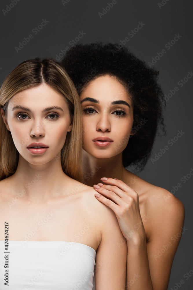 sensual multiethnic women with perfect skin and naked shoulders looking at camera isolated on grey sensual multiethnic women with perfect skin and naked shoulders looking at camera isolated on grey