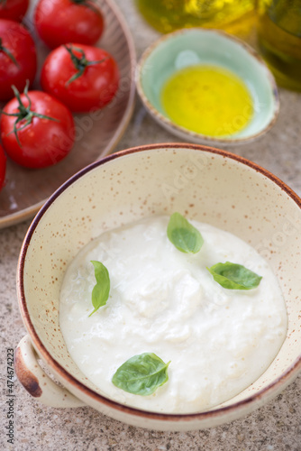 Beige bowl with stracciatella or italian cheese produced from buffalo milk, middle close-up on a beige marble background
