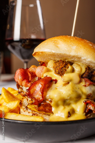 Panino da pub con hamburger di carne, bacon croccante, polpettone fritte, cheddar fuso e patate fritte con un calice di vino rosso sullo sfondo photo