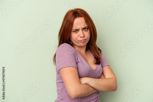 Young caucasian woman isolated on green background frowning face in displeasure, keeps arms folded.