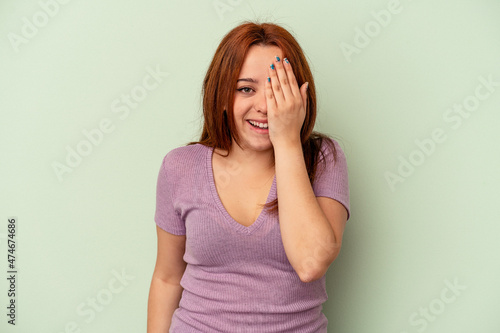 Young caucasian woman isolated on green background having fun covering half of face with palm. © Asier