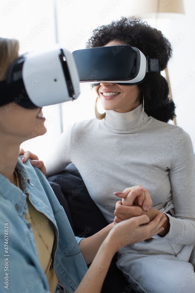 young and happy multiethnic lesbian women gaming in vr headsets while  holding hands at home Stock Photo | Adobe Stock