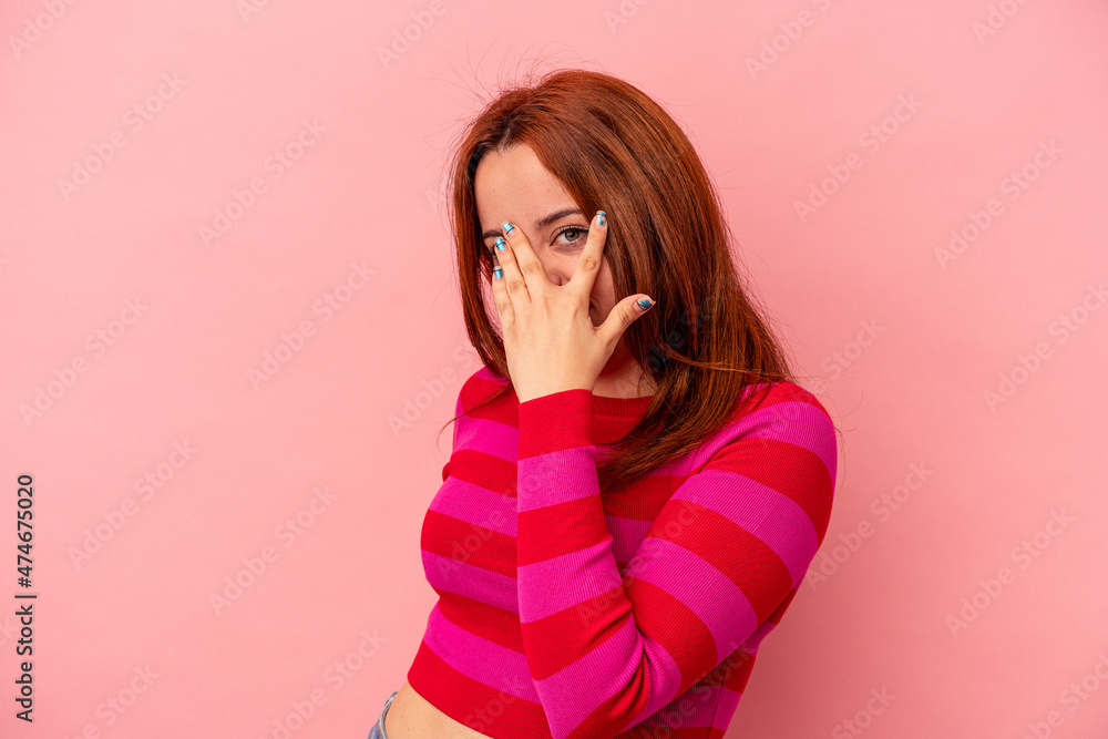 Young caucasian woman isolated on pink background blink at the camera through fingers, embarrassed covering face. Young caucasian woman isolated on pink background blink at the camera through fingers, embarrassed covering face.