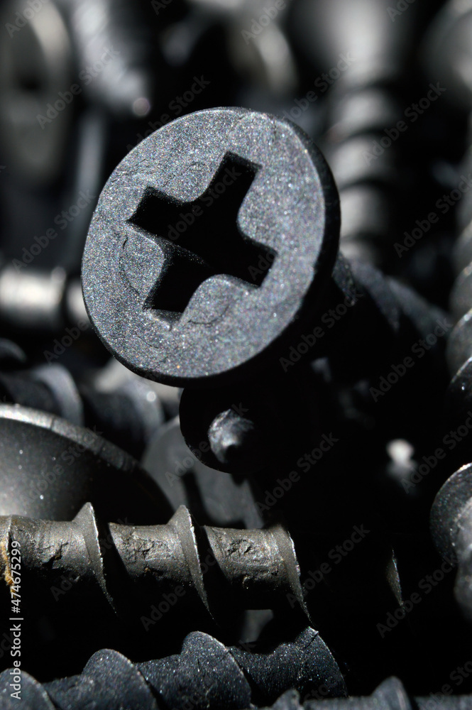 black hardened self-tapping screws lies on a dark background. close-up.