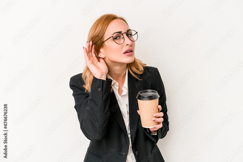 Young business caucasian woman holding take away coffee isolated on white background trying to listening a gossip. Young business caucasian woman holding take away coffee isolated on white background trying to listening a gossip.