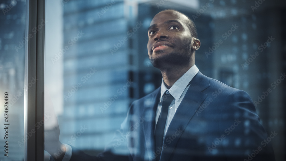 Thoughtful African-American Businessman in a Perfect Tailored Suit Standing in His Office Looking out of the Window on Big City. Successful Investment Manager Planning Strategy. Outside Shot Thoughtful African-American Businessman in a Perfect Tailored Suit Standing in His Office Looking out of the Window on Big City. Successful Investment Manager Planning Strategy. Outside Shot