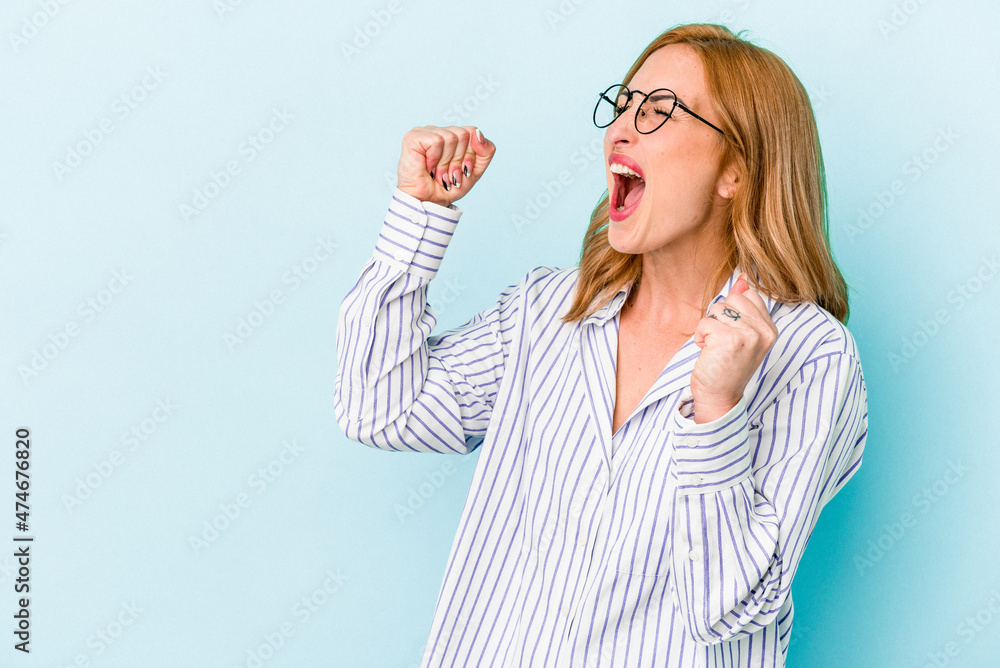 Young caucasian woman isolated on blue background raising fist after a victory, winner concept. Young caucasian woman isolated on blue background raising fist after a victory, winner concept.