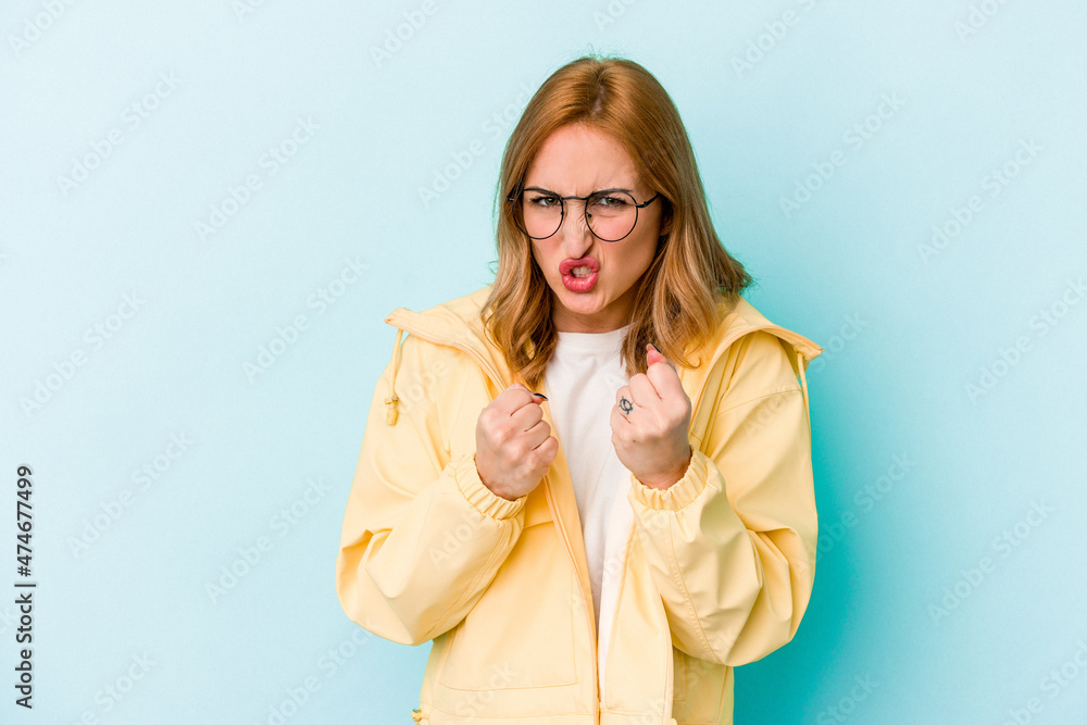Young caucasian woman isolated on blue background showing fist to camera, aggressive facial expression. Young caucasian woman isolated on blue background showing fist to camera, aggressive facial expression.