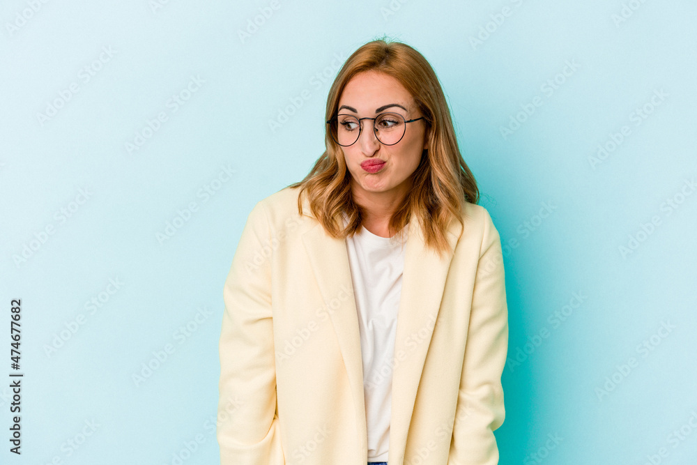 Obraz premium Young caucasian woman isolated on blue background shrugs shoulders and open eyes confused.