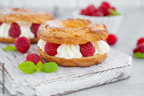 Choux pastries. Choux rings with cream of cream cheese or cottage cheese and fresh raspberries, dusted with powdered sugar on a wooden board on a gray concrete background. photo