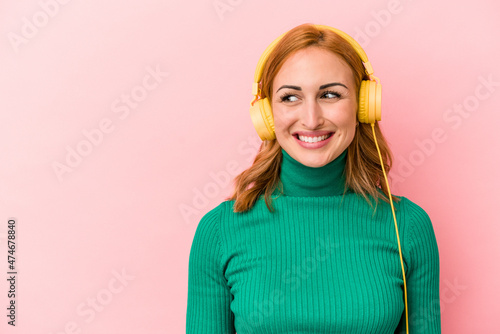 Young caucasian woman listening to music isolated on pink background